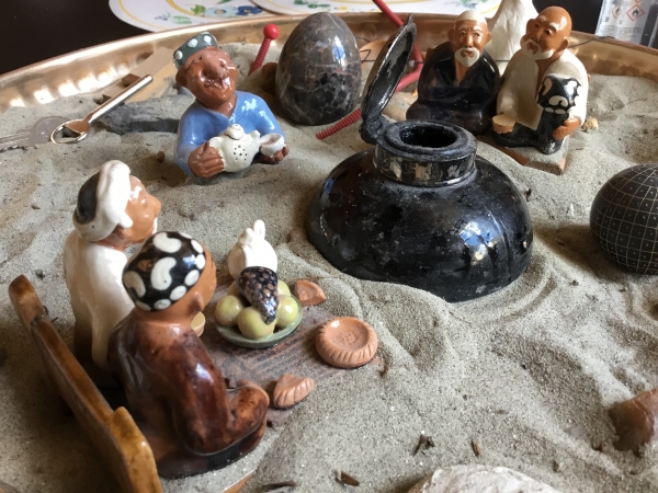 Une scénette composée d’objets de voyage et de figurines, déposée dans un tas de sable du Danube